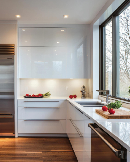 Modern kitchen with glossy custom cabinets, white countertops, large window lighting, and a clean minimalist layout.