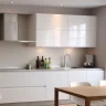 Minimalist white kitchen with handleless cabinets and dining area.